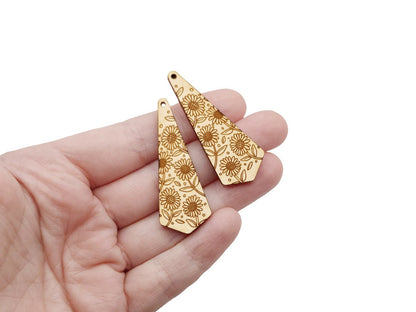 hand holding a pair of two triangle teardrop wood jewelry blanks engraved with a sunflowers pattern