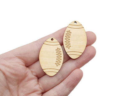 hand holding a pair of two wood jewelry charm blanks cut and engraved to look like a football