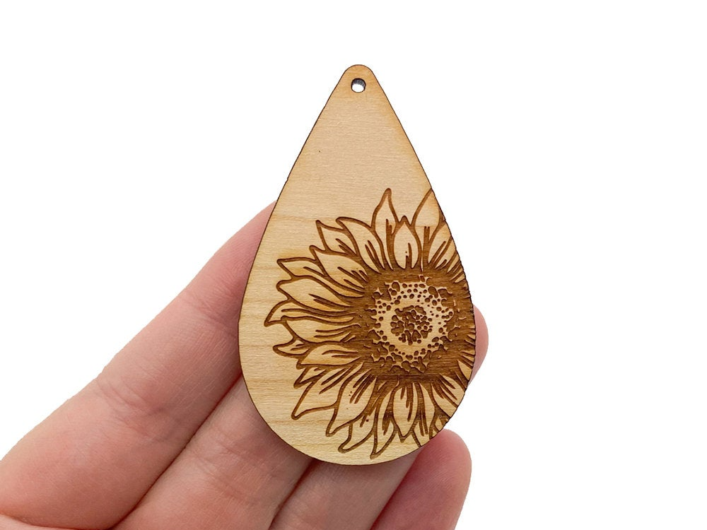 a hand holding a wooden pendant with a sunflower on it