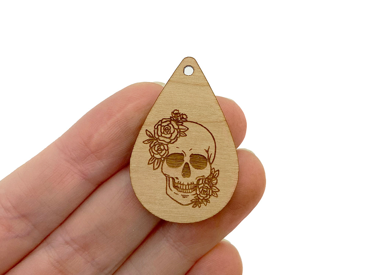 a hand holding a wooden pendant with a skull and roses on it
