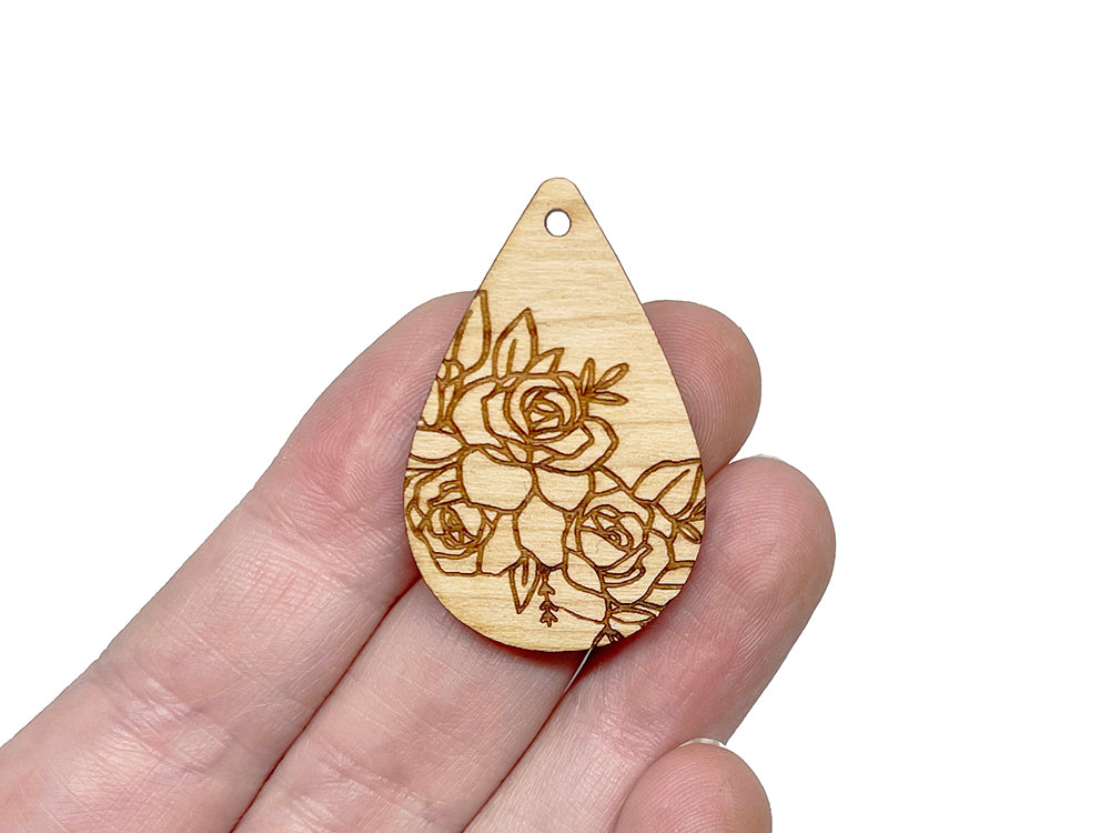 a hand holding a wooden brooch with flowers on it