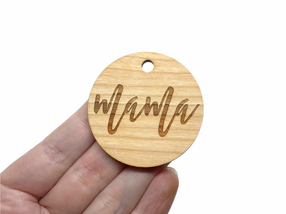 a hand holding a wooden tag with the word mama on it