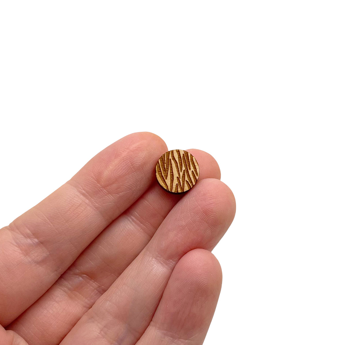 a hand holding a pair of round shaped wooden cabochon stud earring blanks engraved with zebra print
