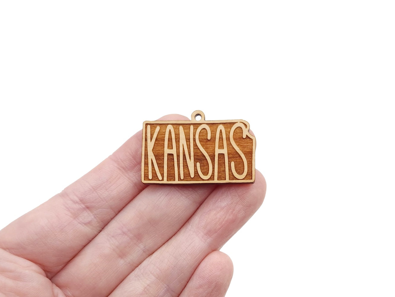a hand holding a small wooden kansas charm