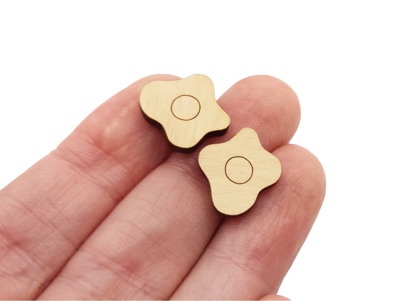 a hand holding a pair of wooden cabochon stud earring blanks cut and engraved to look like fried eggs