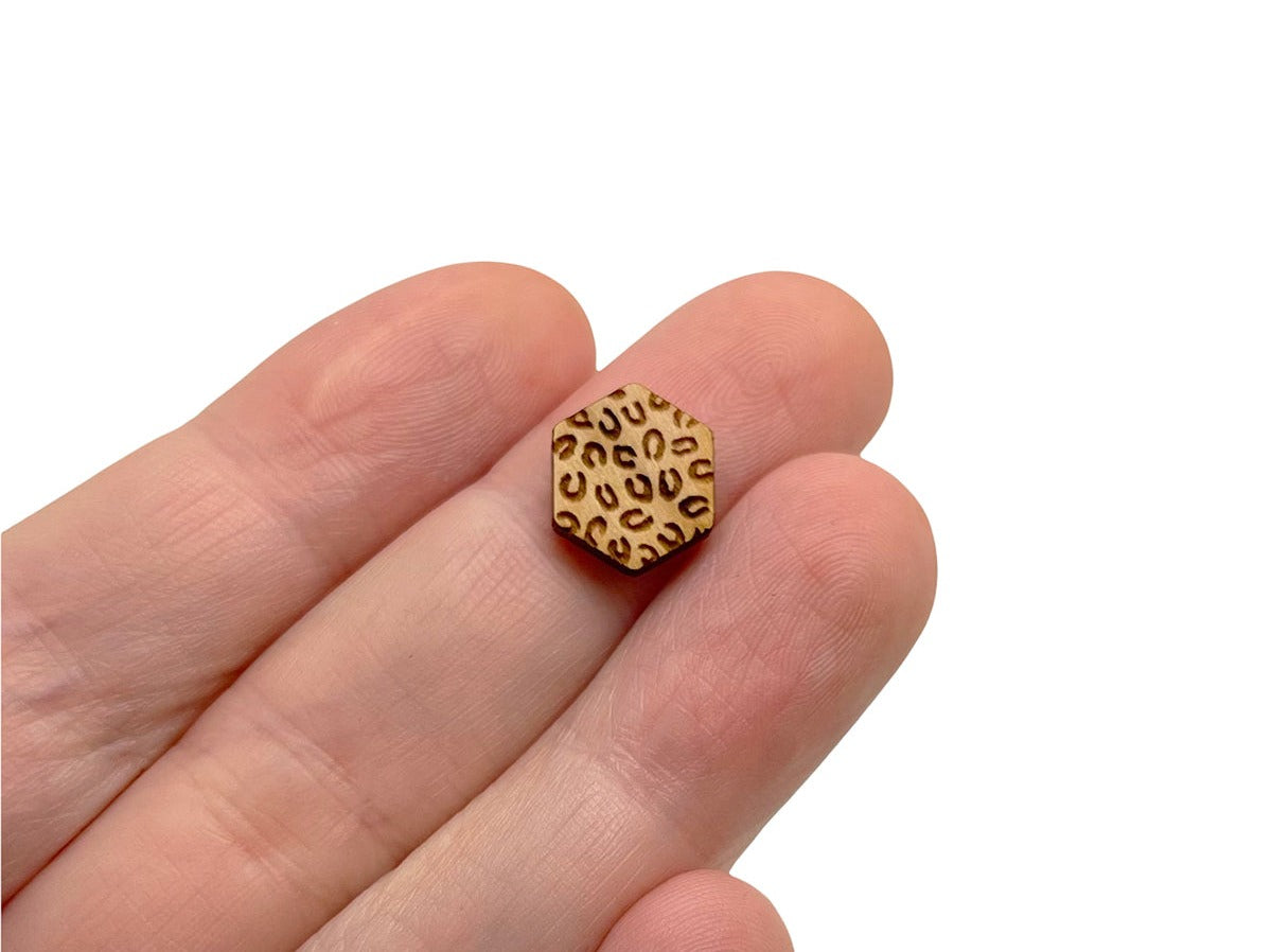 a hand holding a pair of hexagon shaped wooden cabochon stud earring blanks engraved with cheetah print