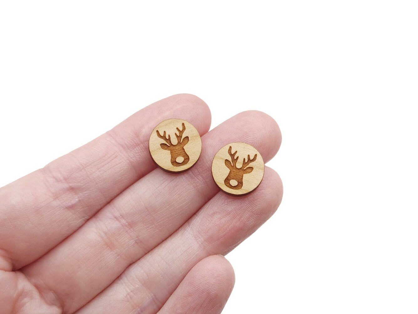 a hand holding a pair of round wooden cabochon earring blanks engraved with a Christmas Reindeer